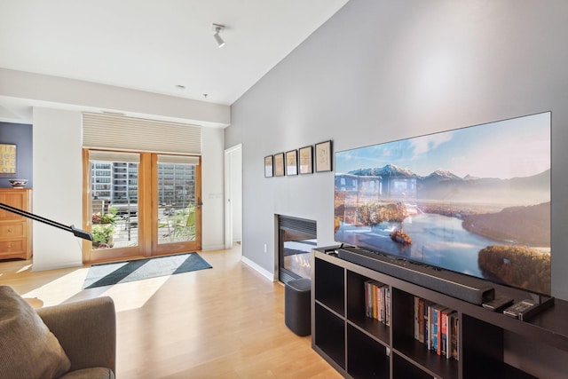 living room featuring light wood-style floors, rail lighting, baseboards, and a glass covered fireplace