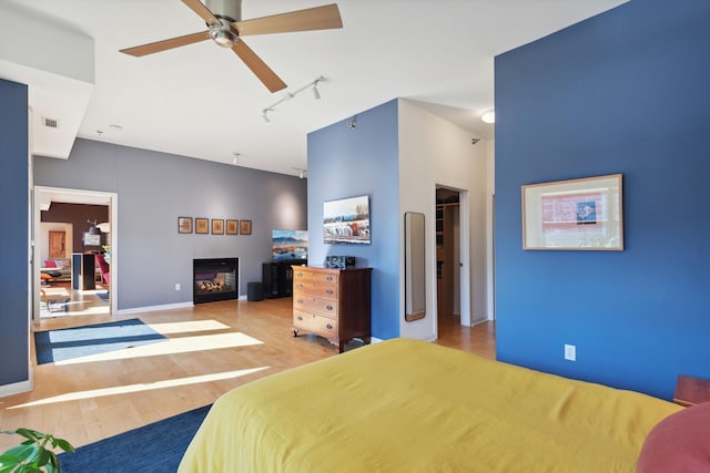 bedroom with ceiling fan, wood finished floors, visible vents, a glass covered fireplace, and track lighting