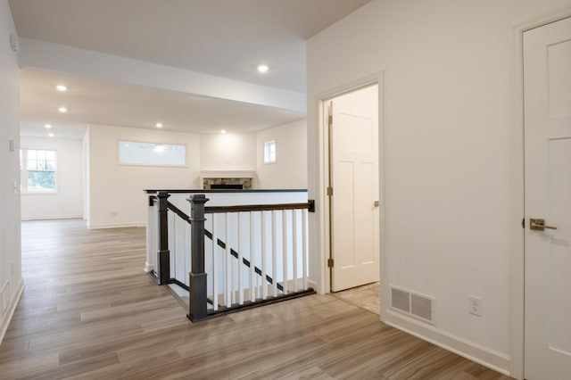 corridor with light wood-type flooring, recessed lighting, visible vents, and an upstairs landing