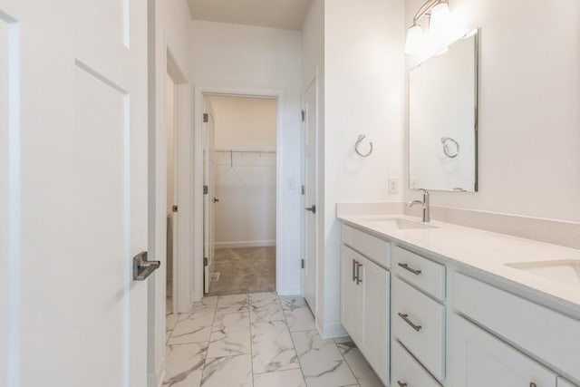 full bathroom featuring marble finish floor, double vanity, a sink, and a walk in closet