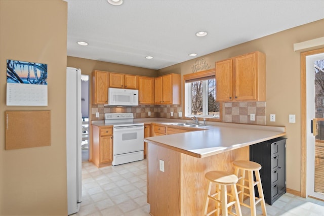 kitchen featuring white appliances, a breakfast bar area, a peninsula, light floors, and a sink