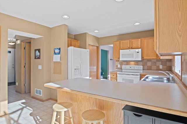 kitchen with white appliances, tasteful backsplash, visible vents, a peninsula, and a sink