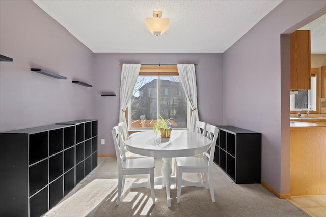 dining room featuring baseboards, a textured ceiling, and light colored carpet