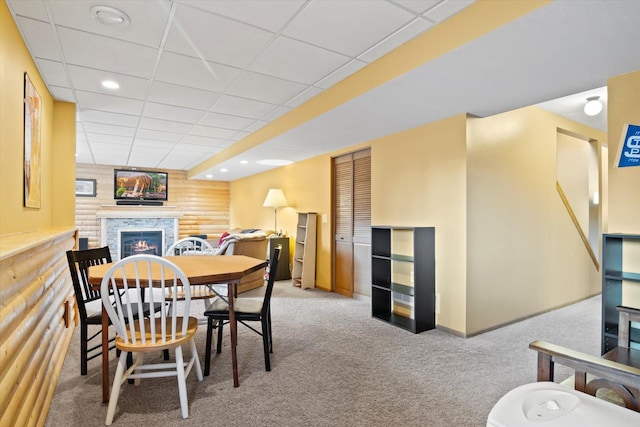 dining area featuring carpet floors, recessed lighting, a warm lit fireplace, and wooden walls