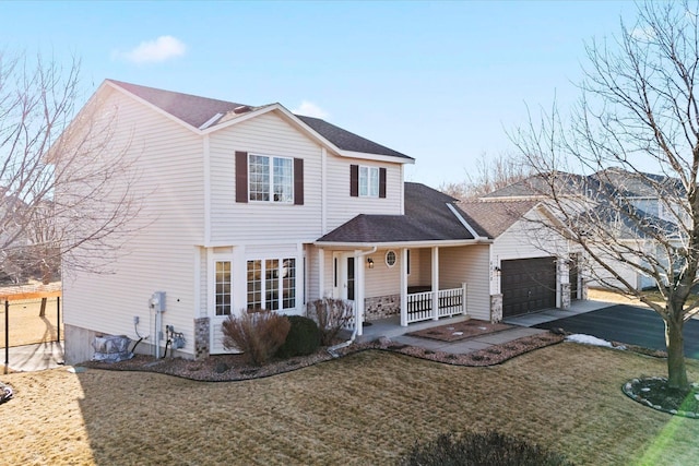 traditional-style home featuring a porch, aphalt driveway, roof with shingles, an attached garage, and a front lawn