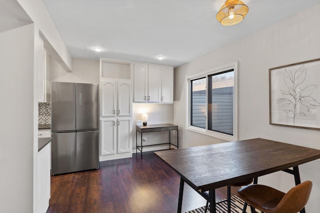 kitchen featuring dark wood-type flooring, freestanding refrigerator, white cabinets, and decorative backsplash