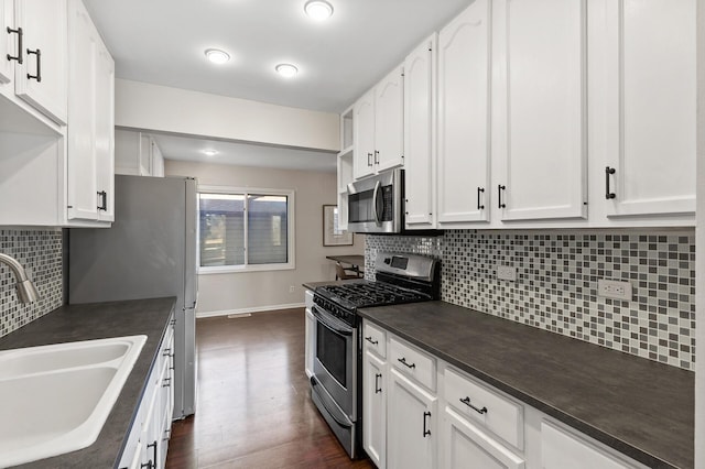 kitchen with stainless steel appliances, dark wood-style flooring, a sink, white cabinets, and dark countertops