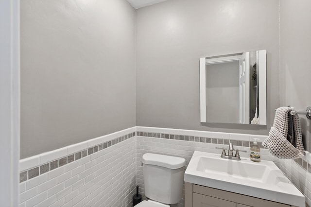 bathroom featuring toilet, wainscoting, tile walls, and vanity