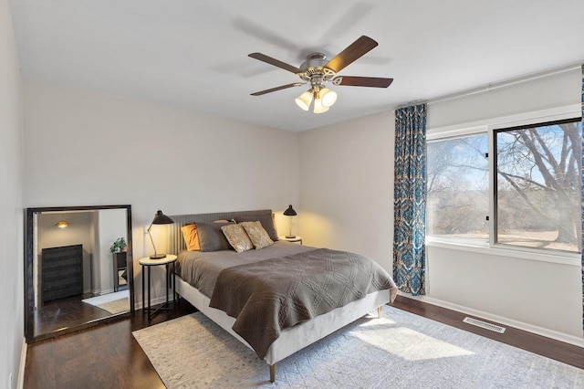 bedroom featuring a ceiling fan, wood finished floors, visible vents, and baseboards