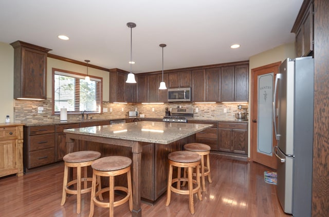 kitchen with a kitchen bar, stainless steel appliances, dark wood finished floors, and a center island