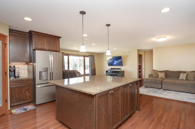 kitchen with light wood finished floors, visible vents, stainless steel fridge with ice dispenser, open floor plan, and a center island