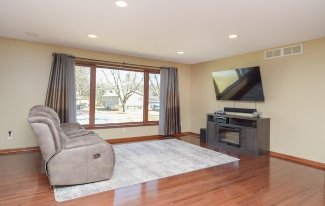 living area with baseboards, visible vents, wood finished floors, and a glass covered fireplace