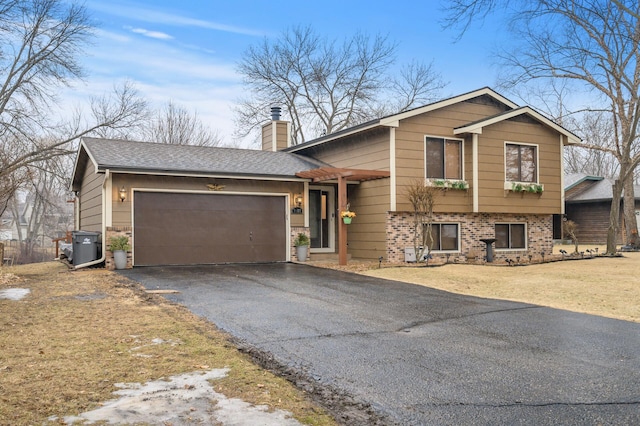 split level home with a front lawn, driveway, an attached garage, a shingled roof, and a chimney