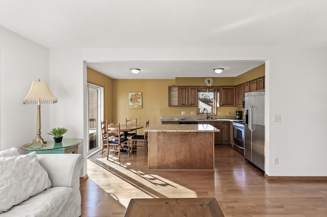 kitchen featuring wood finished floors, open floor plan, appliances with stainless steel finishes, and baseboards