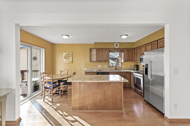 kitchen with brown cabinets, a sink, a center island, light wood-style floors, and appliances with stainless steel finishes