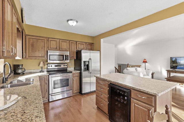 kitchen featuring wine cooler, light wood-type flooring, brown cabinets, appliances with stainless steel finishes, and a sink