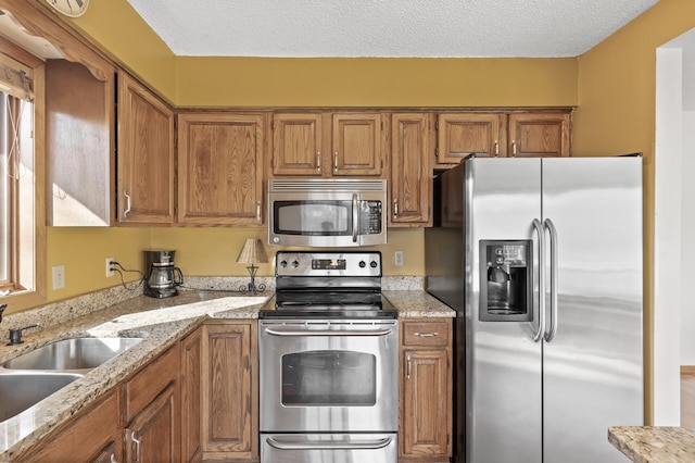 kitchen featuring a sink, a textured ceiling, brown cabinets, and stainless steel appliances