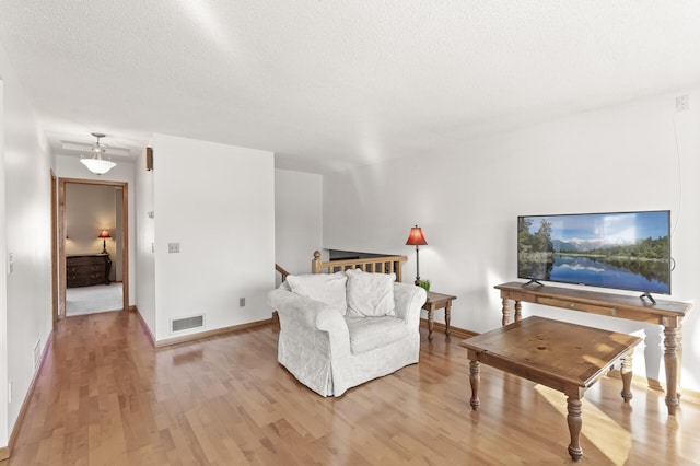 living area with baseboards, light wood-style floors, visible vents, and a textured ceiling