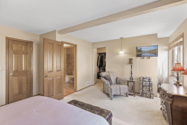 bedroom with a spacious closet, light colored carpet, a closet, ensuite bath, and a textured ceiling