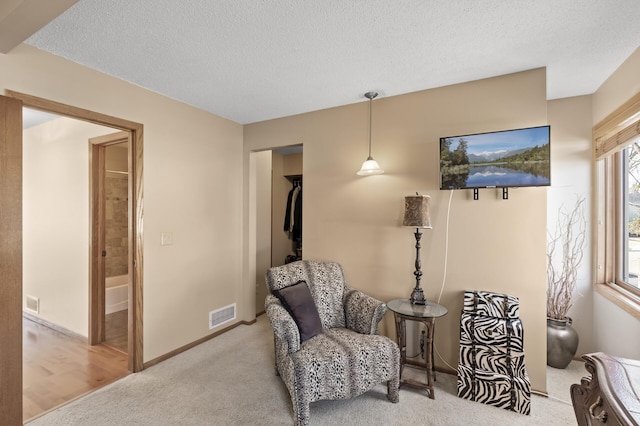 living area with visible vents, carpet floors, a textured ceiling, and baseboards