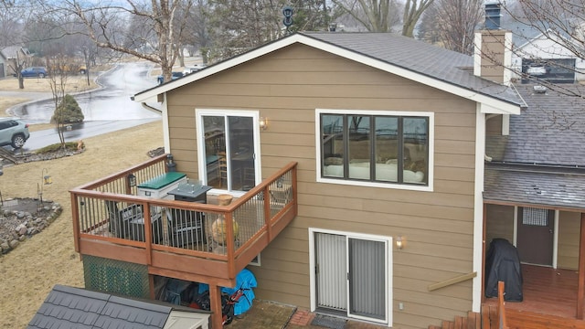 rear view of property with a chimney, roof with shingles, and a wooden deck