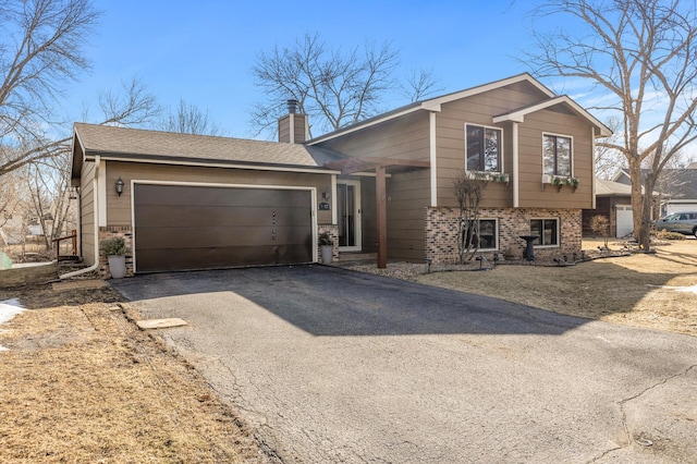 split level home with brick siding, driveway, a chimney, and a garage