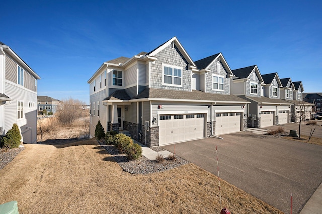 view of front of home featuring stone siding, aphalt driveway, an attached garage, and a residential view