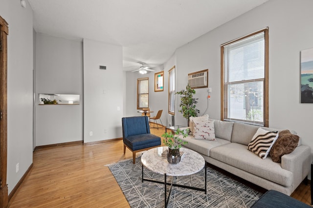 living area featuring light wood finished floors, visible vents, baseboards, a ceiling fan, and an AC wall unit