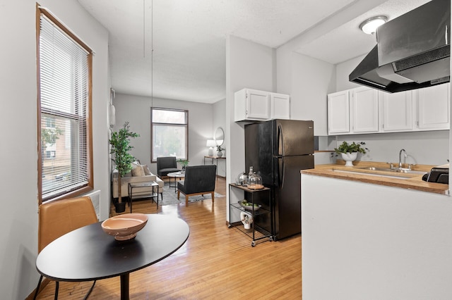 kitchen with light wood finished floors, white cabinets, wood counters, freestanding refrigerator, and range hood