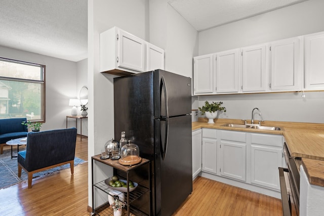 kitchen featuring light countertops, light wood-style floors, freestanding refrigerator, white cabinetry, and a sink