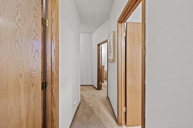 hallway featuring light carpet and baseboards