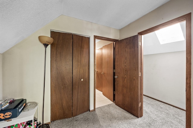 interior space featuring lofted ceiling with skylight, a textured ceiling, a closet, and light colored carpet