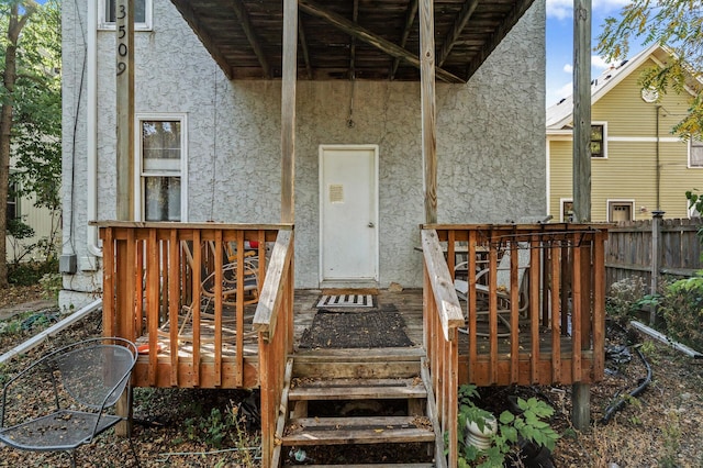 doorway to property featuring fence, a deck, and stucco siding