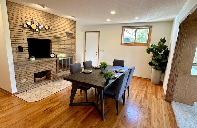 dining room with a fireplace, a textured ceiling, baseboards, and wood finished floors