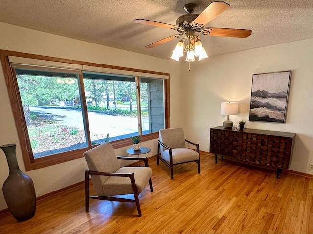 living area featuring a textured ceiling, light wood-style flooring, and ceiling fan