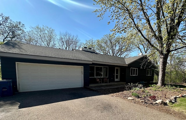 ranch-style house featuring covered porch, driveway, a garage, a chimney, and a shingled roof