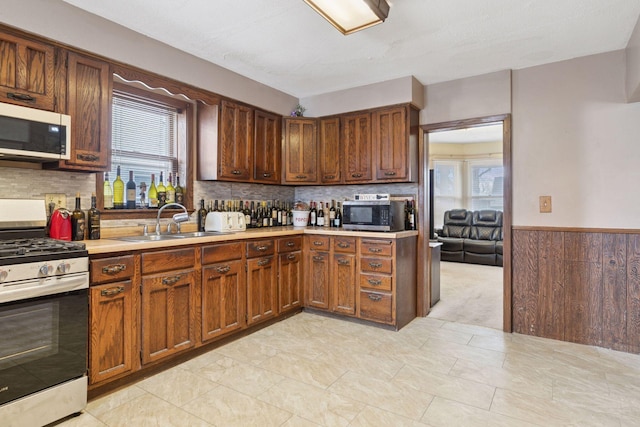 kitchen with a wainscoted wall, stainless steel appliances, wood walls, a sink, and light countertops