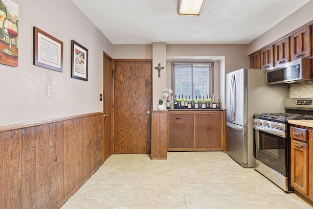 kitchen with appliances with stainless steel finishes, brown cabinetry, wainscoting, and wooden walls