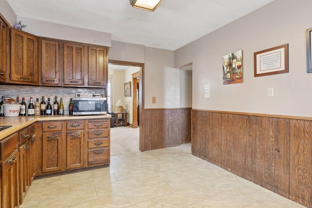 kitchen with brown cabinetry, wainscoting, wooden walls, light countertops, and stainless steel microwave