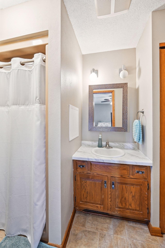 full bathroom with a textured ceiling, curtained shower, vanity, and baseboards