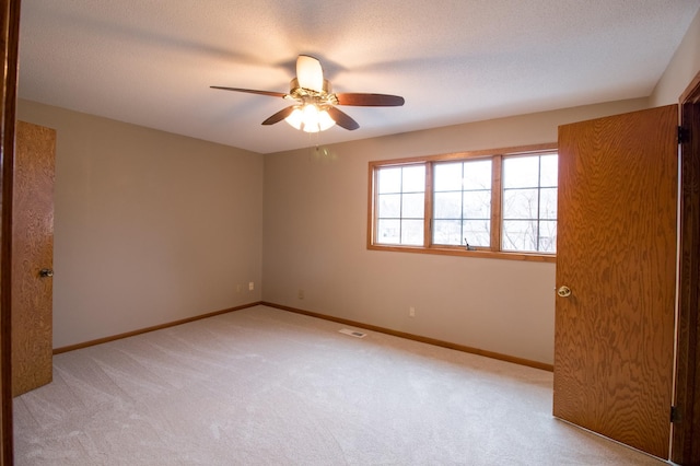 empty room with light carpet, ceiling fan, baseboards, and a textured ceiling