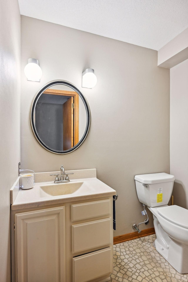 half bath with a textured ceiling, vanity, toilet, and baseboards