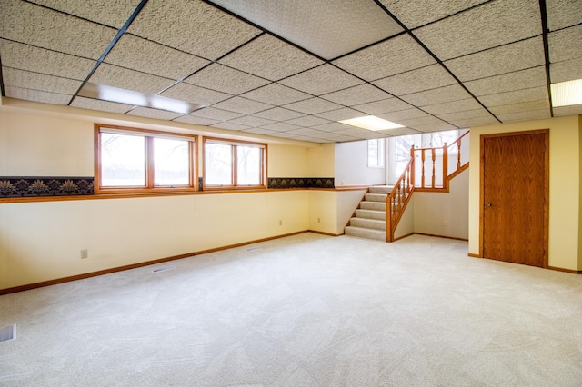 below grade area with a paneled ceiling, visible vents, stairway, carpet flooring, and baseboards