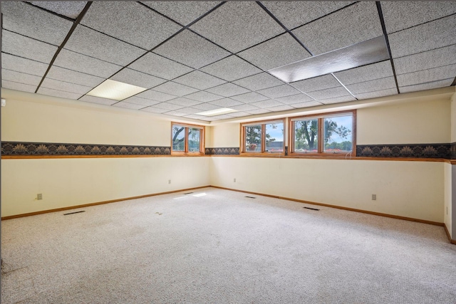 carpeted empty room with wainscoting, a drop ceiling, visible vents, and baseboards