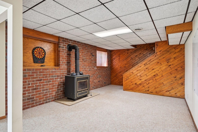 finished basement featuring a wood stove, wood walls, carpet, and visible vents