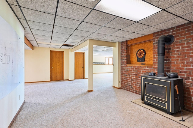 unfurnished living room with carpet floors, a paneled ceiling, a wood stove, and baseboards