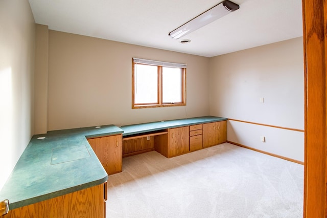 unfurnished office with visible vents, light colored carpet, built in desk, and baseboards