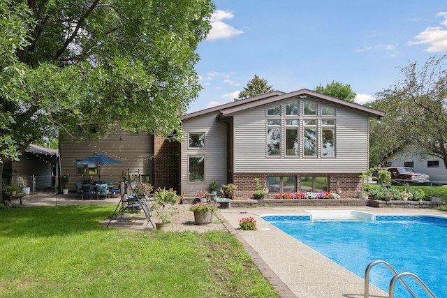 rear view of property with a yard, brick siding, an outdoor pool, and a patio