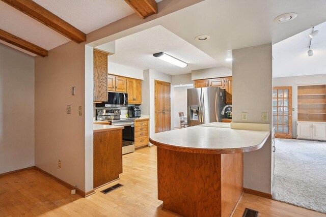 kitchen featuring appliances with stainless steel finishes, light countertops, a peninsula, beam ceiling, and light wood-style flooring