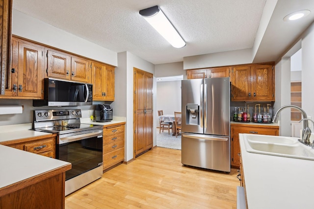 kitchen with appliances with stainless steel finishes, brown cabinets, light countertops, light wood-style flooring, and a textured ceiling